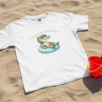 White t-shirt with a graphic of a crocodile and text 'Floating & Unbothered' on sand